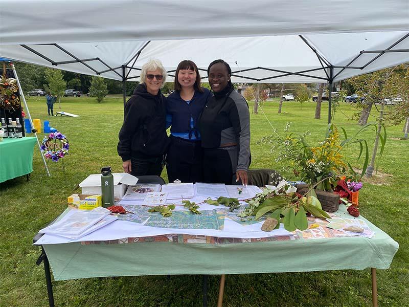 Three women in mile market showing maps of food forests